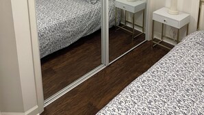 Un dormitorio con cama, mesita de noche con lámpara, espejo y un cuadro en la pared.