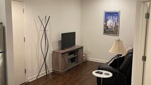 Una sala de estar con televisor, sofá, mesa de centro y lámpara.