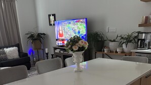 Una sala de estar moderna con una mesa de comedor blanca, un sofá, un televisor y plantas en macetas.