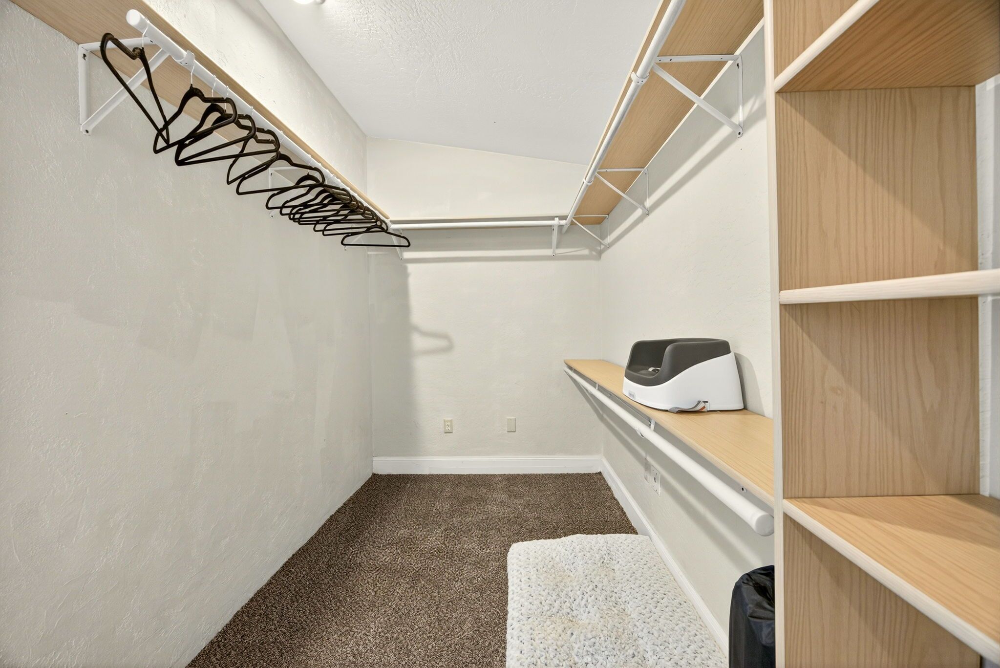 A small, well-lit closet with a hanging rack, shelves, and a bench.