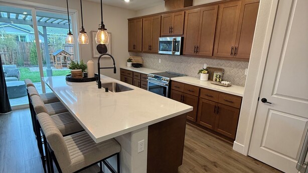 A modern kitchen with a large island, wooden cabinets, stainless steel appliances, and pendant lighting.