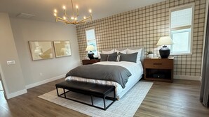 A bedroom with a large bed, bedside tables, a chandelier, and a window with blinds.