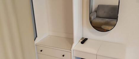 A small, white room with a dresser, a mirror, and a hanging garment rack.