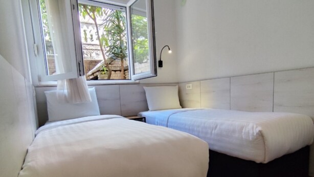 A bedroom with two beds, a window with a view of greenery, and a wall-mounted light fixture. - Comfort Apartments Igalo 60 m From the Sea (Igalo)
