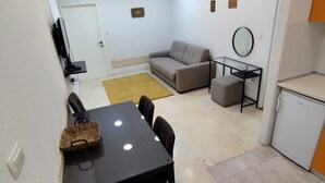 A compact living space with a dining table, chairs, a sofa, a small ottoman, a TV, a mirror, and a refrigerator. - Comfort Apartments Igalo 60 m From the Sea (Igalo)