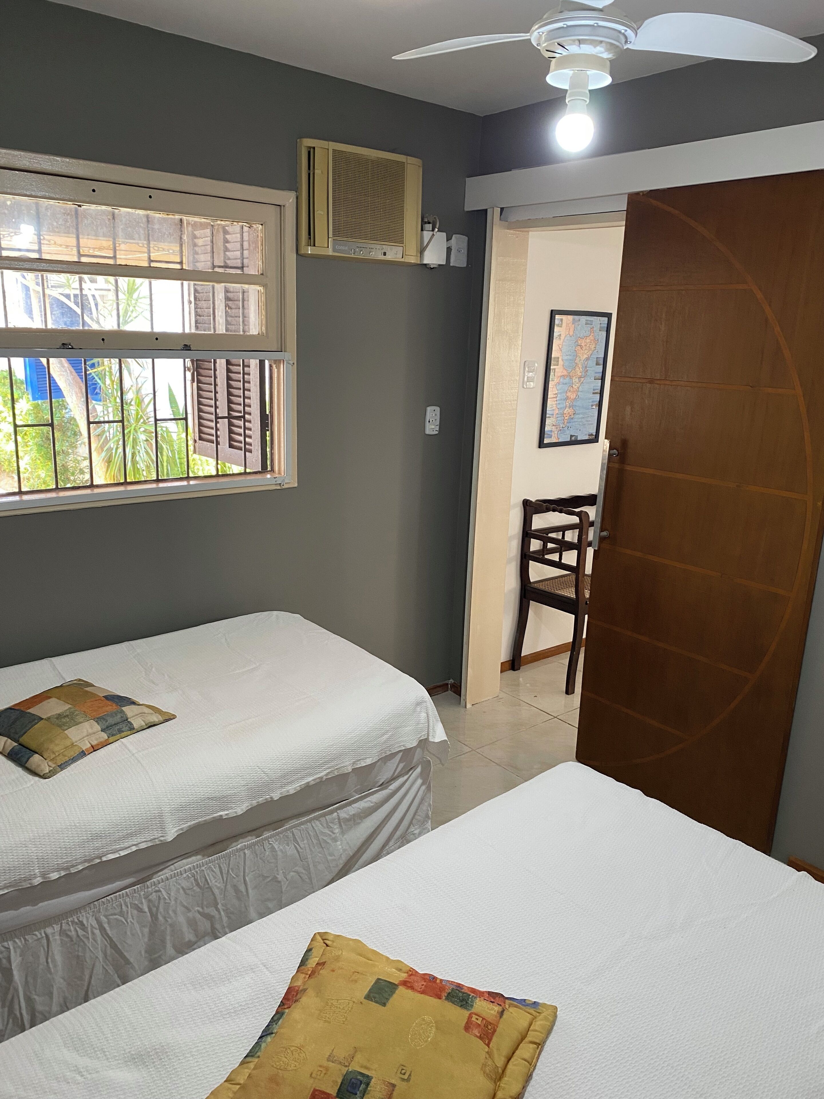 A room with two beds, a ceiling fan, a window with bars, and a map on the wall.