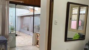Une pièce dotée d’une porte-fenêtre coulissante donnant sur un espace extérieur, d’une petite table recouverte d’une nappe à carreaux et d’un miroir au mur.