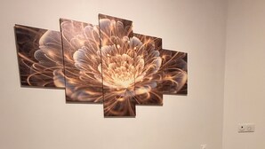 Une pièce dont un mur est orné d’une œuvre d’art composée de plusieurs panneaux et représentant une fleur. On y trouve une petite table sur laquelle sont posés un set de table en fibres tressées et une boîte à mouchoirs.