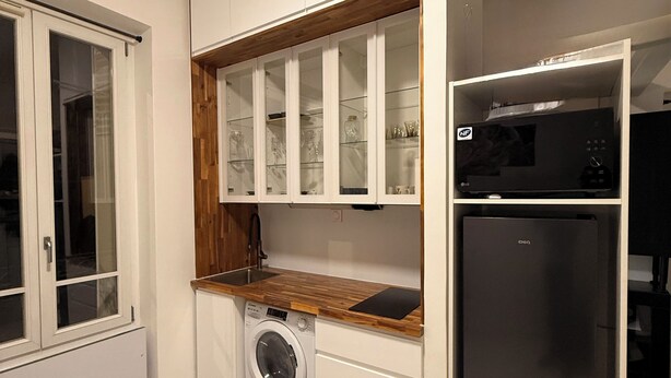 Une cuisine compacte dotée d’un lave-linge encastré, d’un réfrigérateur noir et d’un plan de travail en bois.