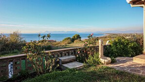 A stone pathway leading to a terrace overlooking a coastal landscape with mountains in the distance.