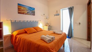 A bedroom with an orange bedspread, a painting of a sunset, a fish decoration, and a door with curtains.