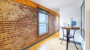 A hallway with exposed brick walls, a wooden ceiling, and a round table with a sign. - Urban Brick Loft Studio • Ride to Trails • Walk to Dining, Shops & Nightlife (Rogers)