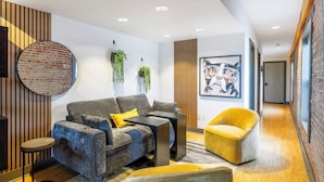 A modern living room with a grey sofa, yellow armchair, and a round brick wall accent. - Urban Brick Loft Studio • Ride to Trails • Walk to Dining, Shops & Nightlife (Rogers)