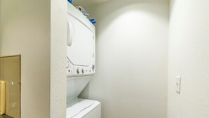A laundry room with a white washing machine and dryer, a wooden cabinet, and a white wall. - Urban Brick Loft Studio • Ride to Trails • Walk to Dining, Shops & Nightlife (Rogers)
