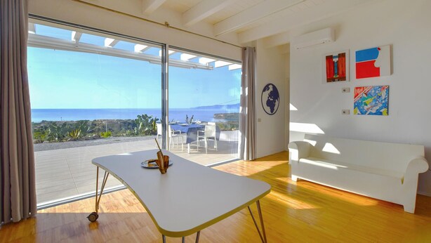 A modern room with a large sliding glass door leading to a terrace with a view of the sea.