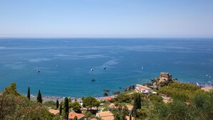 A coastal town with a historic castle, clear blue sea, and beach with umbrellas.