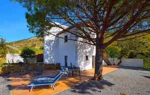 Un edificio blanco con un patio, mobiliario exterior y un árbol.