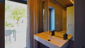 Un baño moderno con un lavamanos blanco, un espejo y vistas a un árbol desde el exterior.