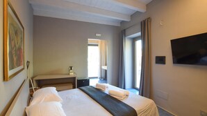 Una habitación de hotel con cama, escritorio, silla, televisor y ventana con cortinas.