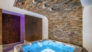 Moderni spa-huone, jossa on kiviseinä, poreallas ja violetilla valolla valaistu seinä.