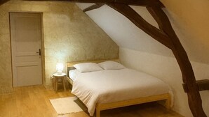 A bedroom with a wooden bed, a nightstand, a lamp, and a door. - La Bergerie des vignes" country house shared with sheep. (Bourgueil)