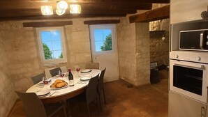 A rustic kitchen with a dining table set for two, a built-in oven, and a window with a view of trees. - La Bergerie des vignes" country house shared with sheep. (Bourgueil)