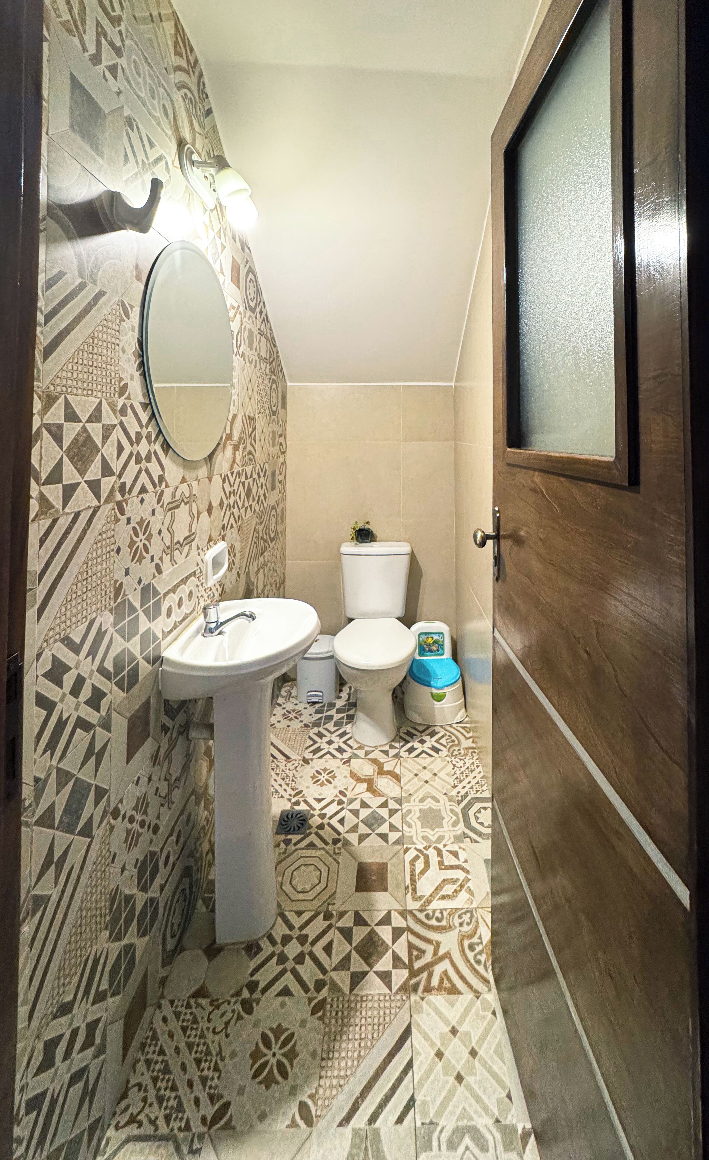 Une salle de bain avec un sol carrelé à motifs, un lavabo blanc, des toilettes et un miroir.
