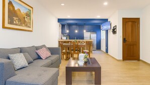 Ein Wohnzimmer mit grauem Sofa, einem Couchtisch mit Vase sowie einem Essbereich mit Holztischen und -stühlen.