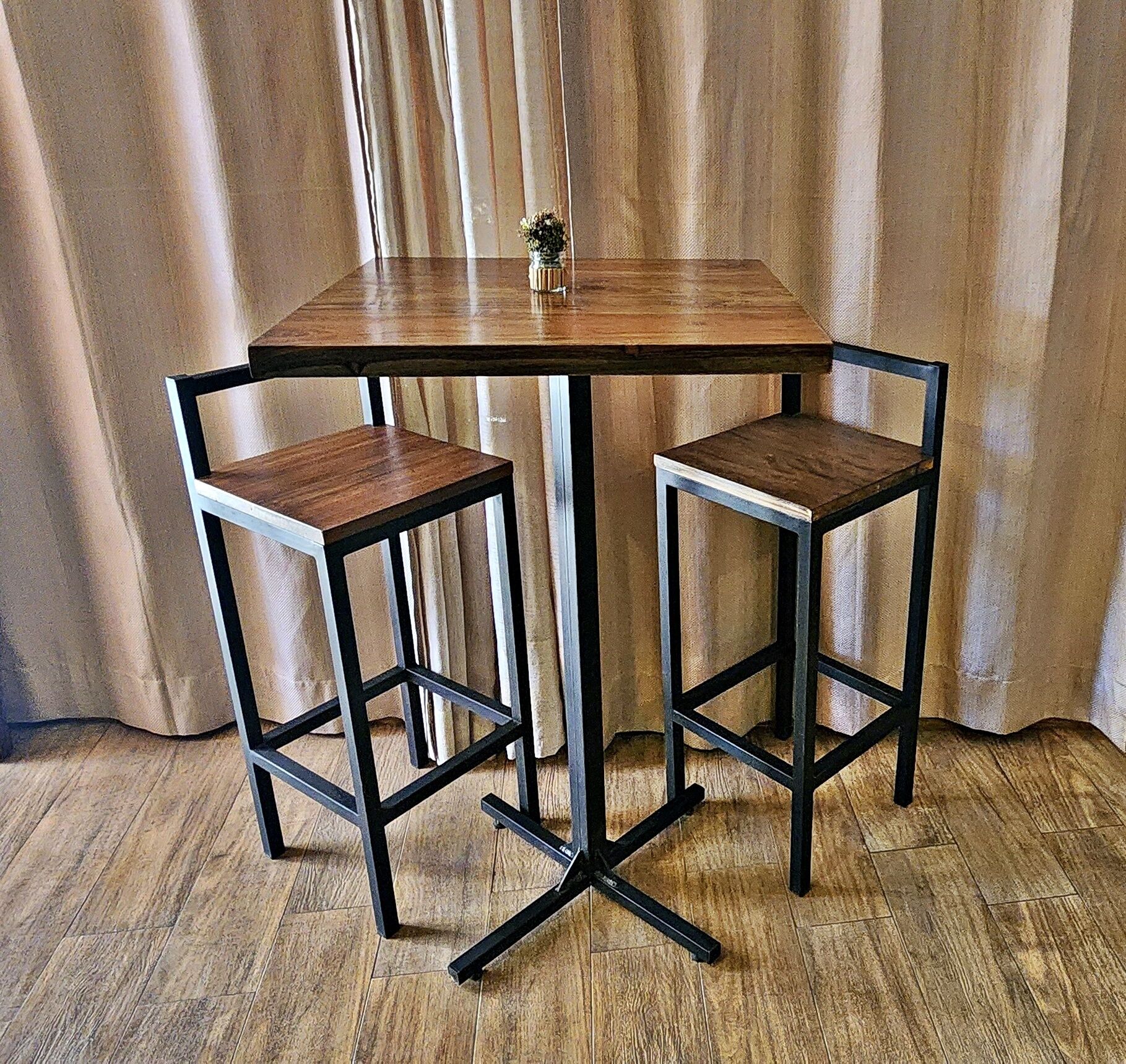 A rectangular table with a wooden top and black metal frame, flanked by two matching stools with wooden seats and metal legs.