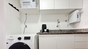 A compact kitchen with a washing machine, a microwave, and a coffee maker. - Studio apartment with movement, elevator, and open balcony in Asa Norte. (Brasília)