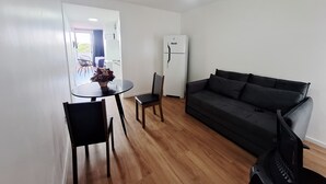 A compact living space with a round dining table, two chairs, a black sofa, and a white refrigerator. - Studio apartment with movement, elevator, and open balcony in Asa Norte. (Brasília)