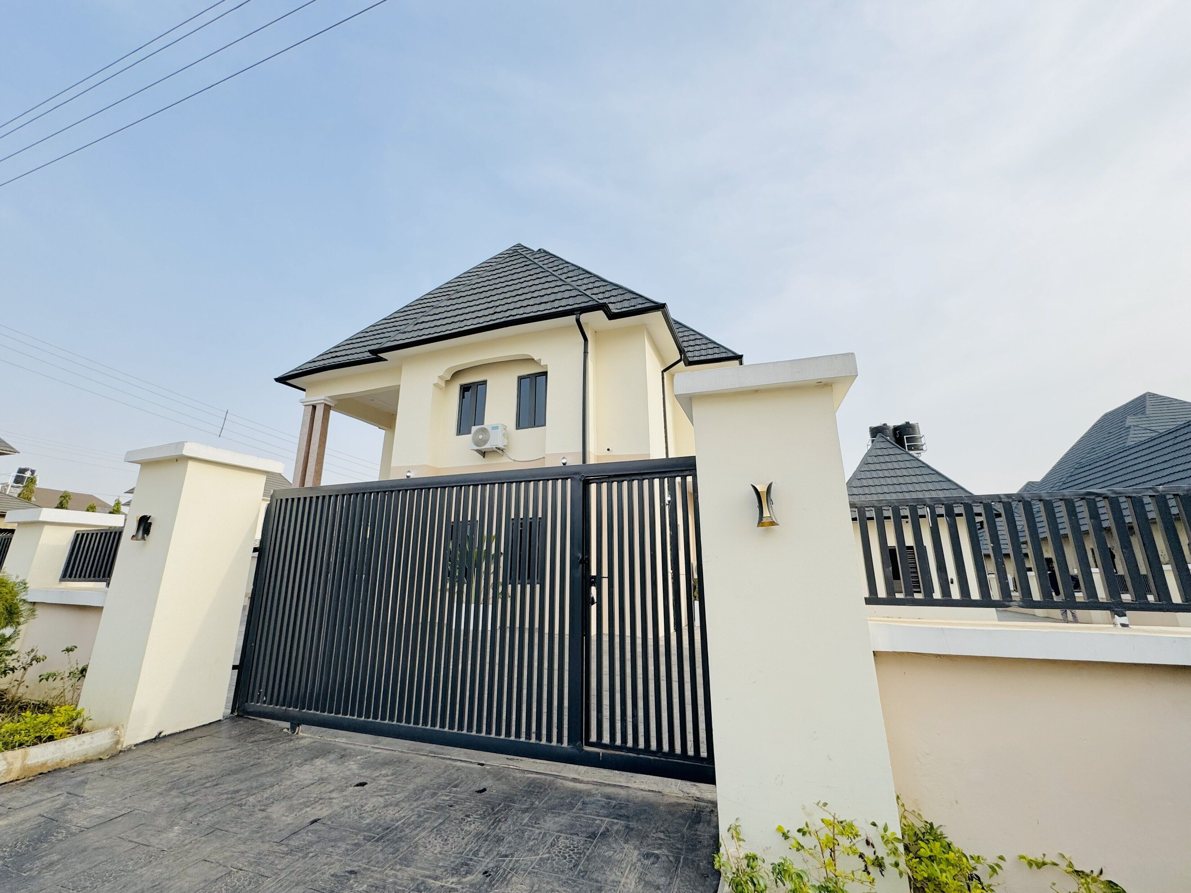 A gated residential area with a modern house featuring a flat roof and a black metal gate.