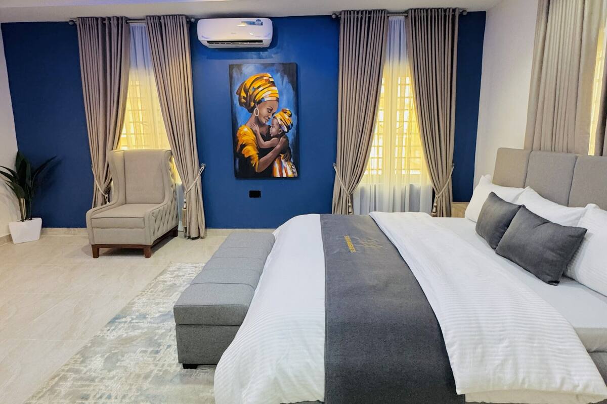 A modern bedroom with a large bed, a painting on the wall, and a ceiling light.