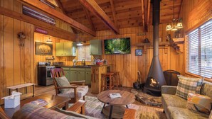 A cozy cabin interior with wooden walls, a stone fireplace, a television, and a kitchen area. - Cozy country cabin in Big Bear perfect for your getaway. Pets wifi. New spa. (Big Bear)