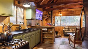 A rustic kitchen with wooden cabinets, a stove, and a television mounted on the wall. - Cozy country cabin in Big Bear perfect for your getaway. Pets wifi. New spa. (Big Bear)