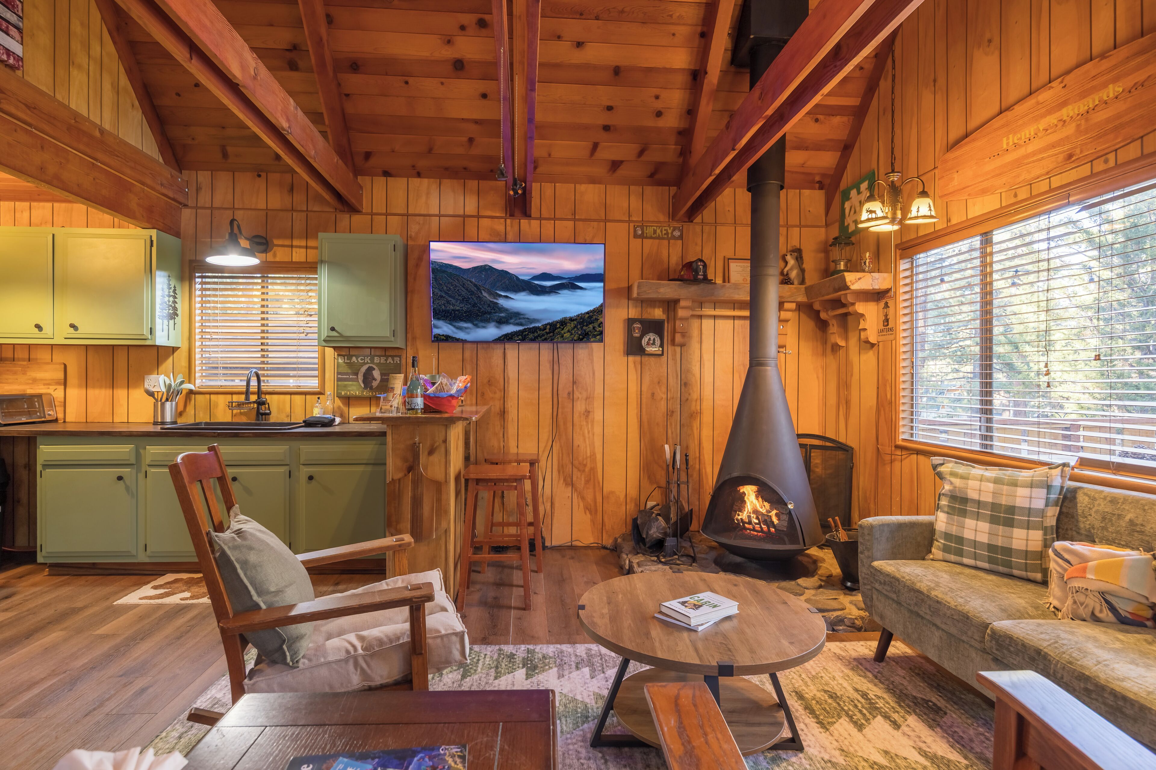 A cozy cabin interior with wooden walls, a stone fireplace, a dining area, and a comfortable seating space.