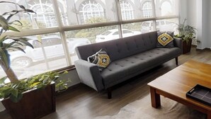 Una sala de estar moderna con un sofá gris, una mesa de centro de madera y grandes ventanales con vistas a la calle.