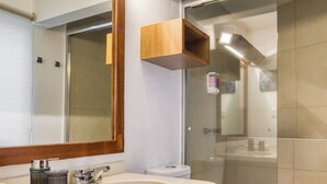 Un baño moderno con tocador de madera, un espejo grande, un lavamanos y un inodoro.