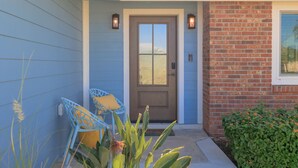 A house with a blue exterior, a brown front door, and a brick section. There are two blue chairs with yellow cushions outside. - Clover Vacation Homes: Snead Island: Luxury 4 BR, Heated Pool, Beaches (Palmetto)