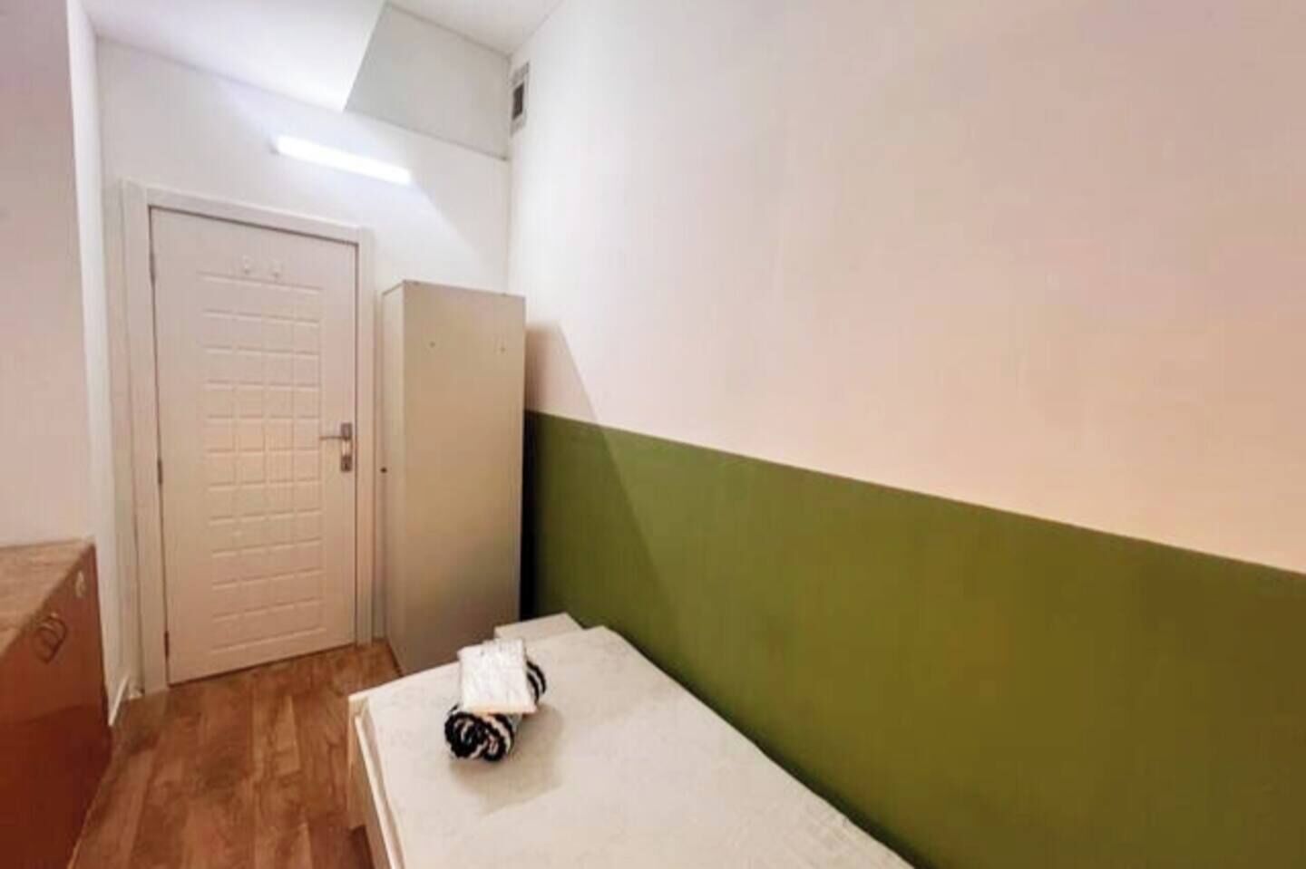 Une petite pièce étroite, avec un plancher en bois, une porte blanche et un mur vert.