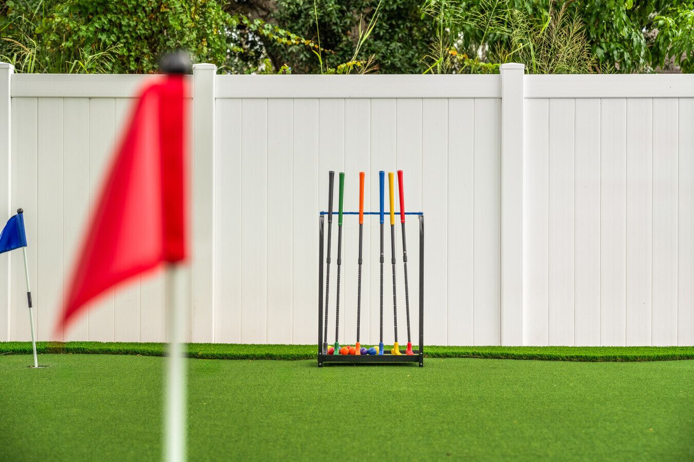 Un espace d’entraînement de golf avec une clôture blanche, un drapeau rouge et un emplacement de départ équipé de clubs de golf.