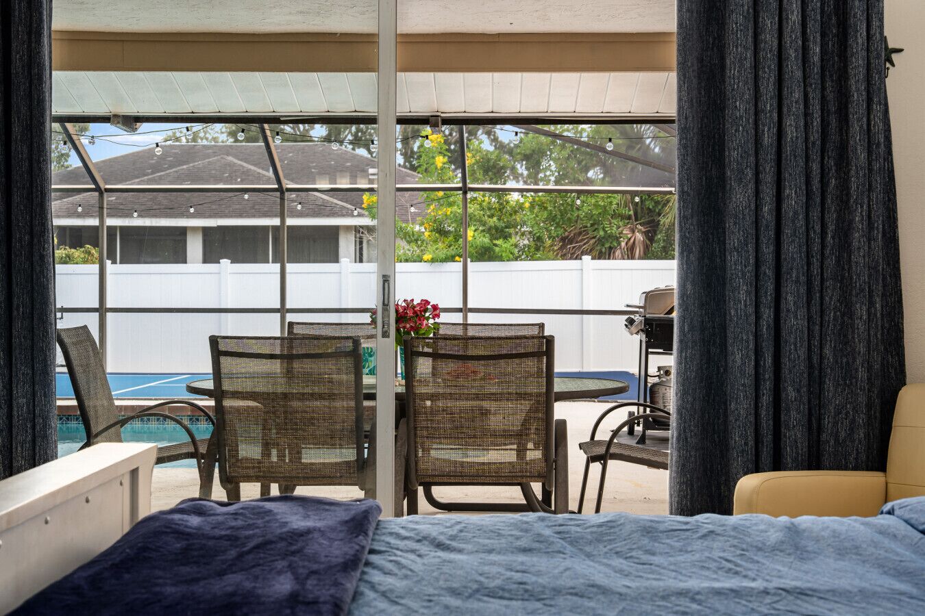 A bedroom with a bed, a window overlooking a pool and outdoor furniture.