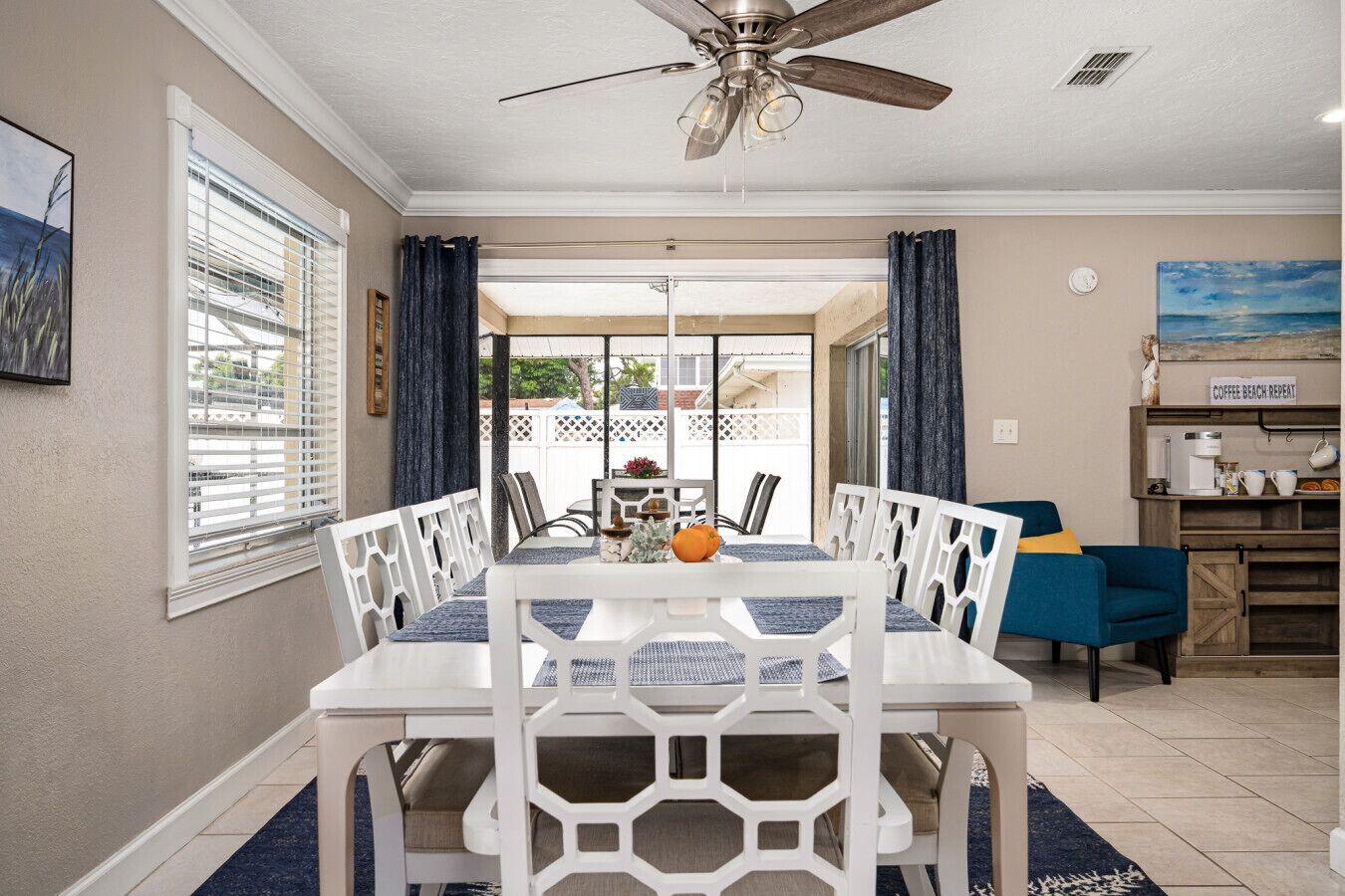 A dining area with a white table and chairs, a ceiling fan, and a view of the backyard through glass doors.