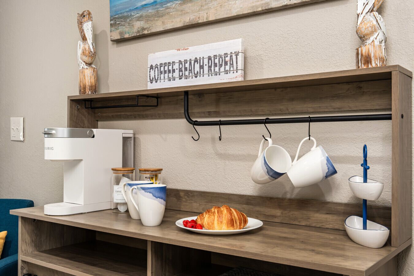 A coffee station with a coffee maker, mugs, and a croissant on a wooden counter.