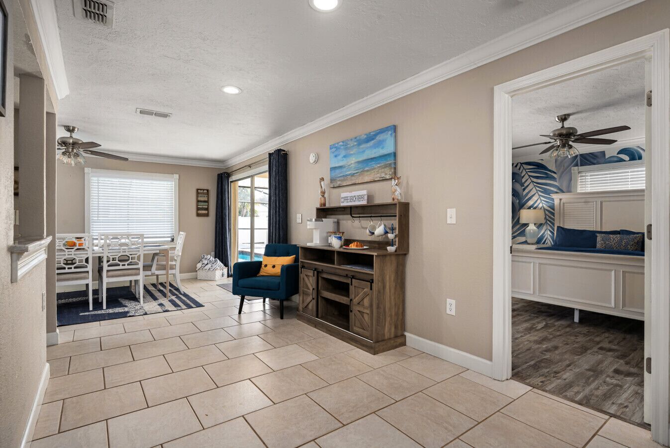 A spacious living area with a dining table, chairs, a blue armchair, a coffee station, and a view of the outdoors.