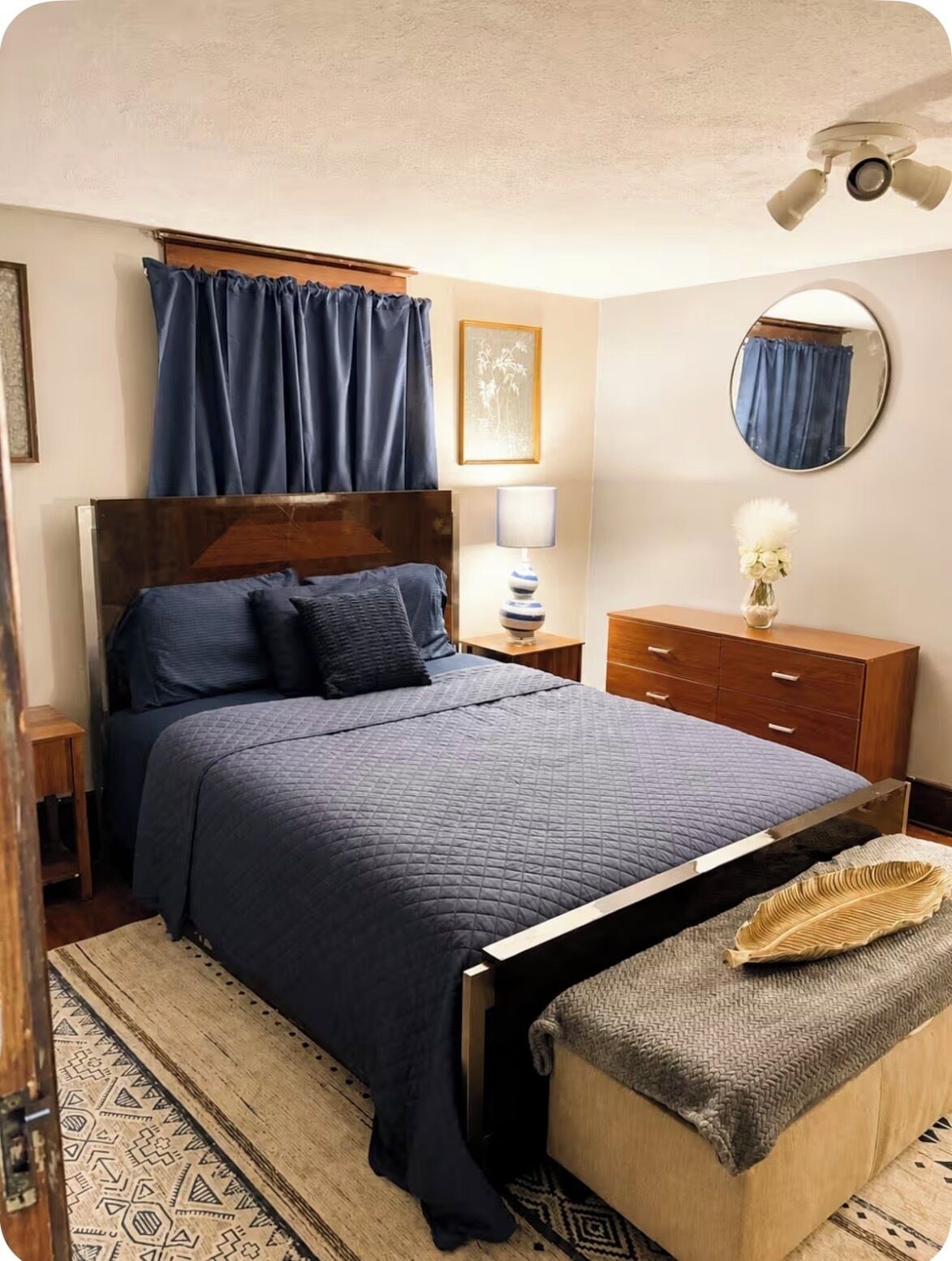 Une chambre à coucher comprenant un lit, une table de chevet, une commode, un miroir et un ventilateur de plafond.