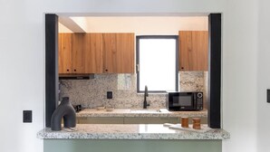 A modern kitchen with wooden cabinets, granite countertops, a black microwave, and a window. - Baranda OCHO By Smart W (Mexico City)