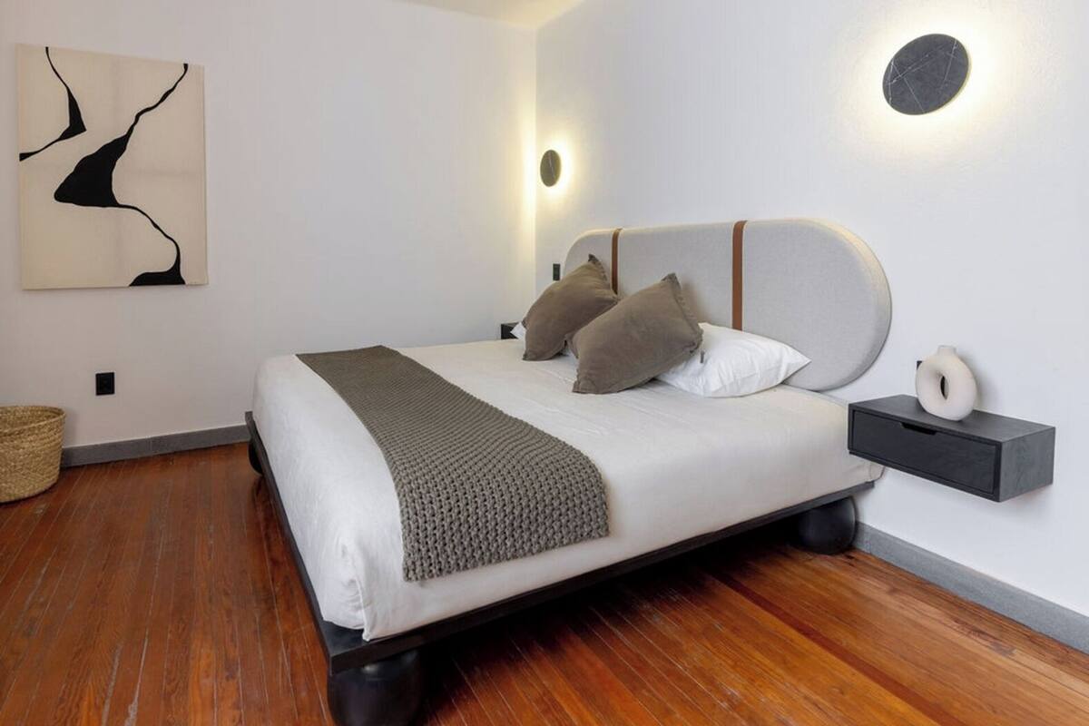 A modern bedroom with a bed, pillows, a bedside table, and a wall-mounted light fixture.