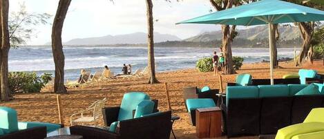 A beachside seating area with outdoor furniture and umbrellas, overlooking the ocean.