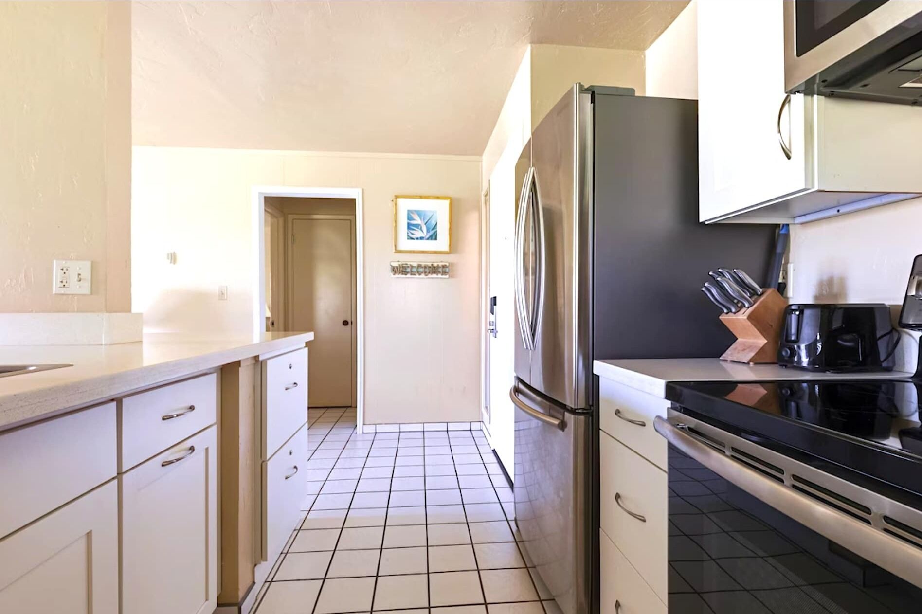 A kitchen with white cabinets, a stainless steel refrigerator, a stove, and a coffee maker.